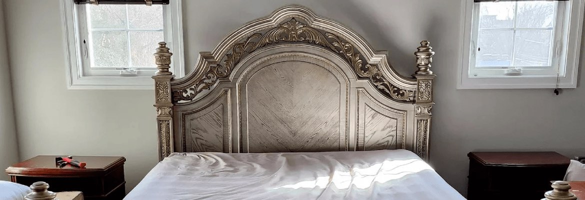 A king bed with an ornate headboard, assembled and made up in a bright bedroom