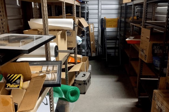Storage room crowded with metal shelving, boxes and loose items