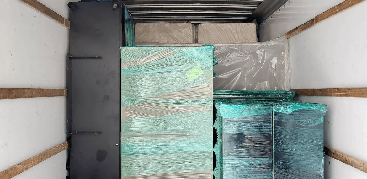 Dressers in green and clear stretch wrap packed against the front wall of a truck